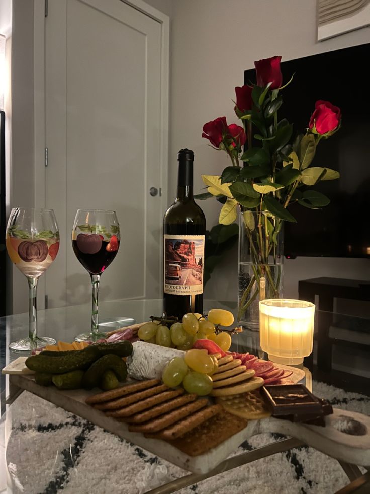 a table with wine, cheese and crackers next to a vase filled with roses