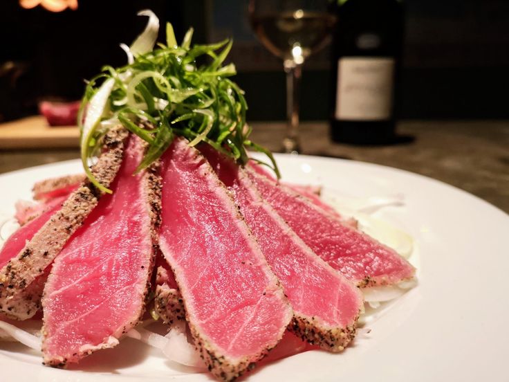 a white plate topped with meat and veggies next to a bottle of wine