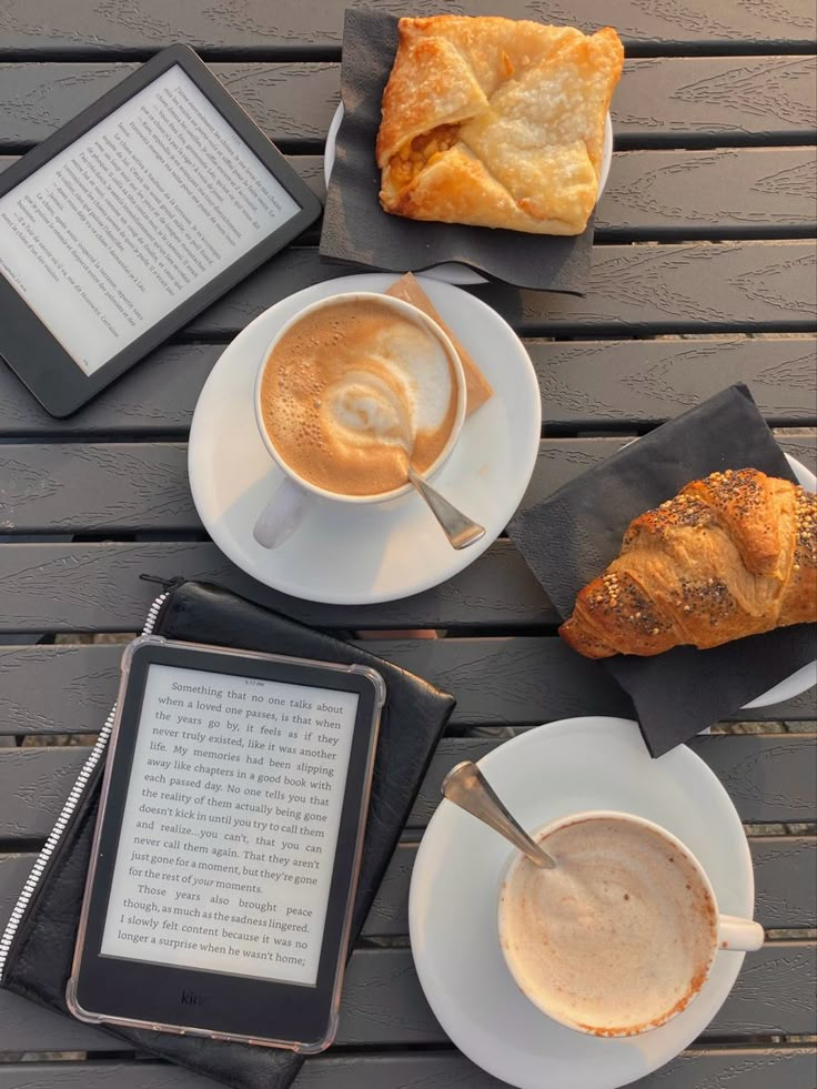 there is a cup of coffee and an ipad on the table next to some croissants