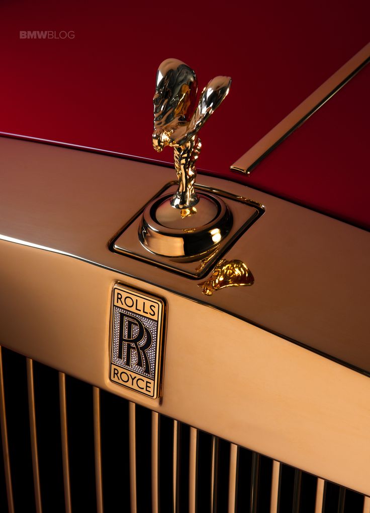 the hood ornament on an old rolls royce car is gold and has a red background