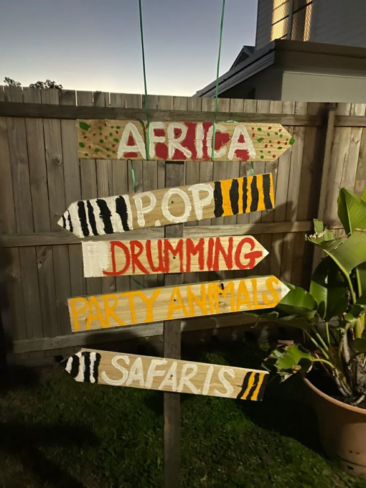 a wooden sign that has various signs on it in front of a fence with plants