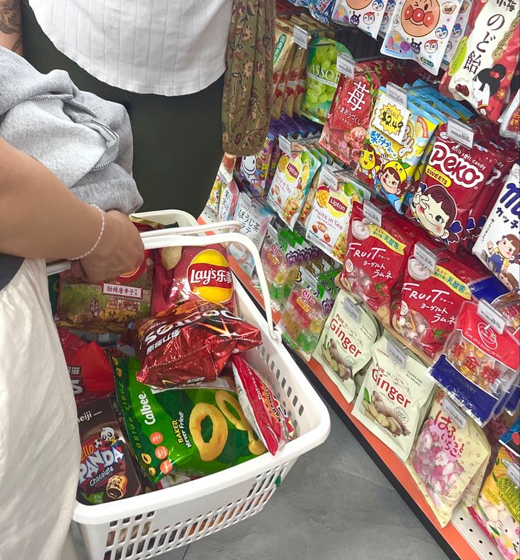 a person holding a shopping basket in front of a store shelf filled with food items