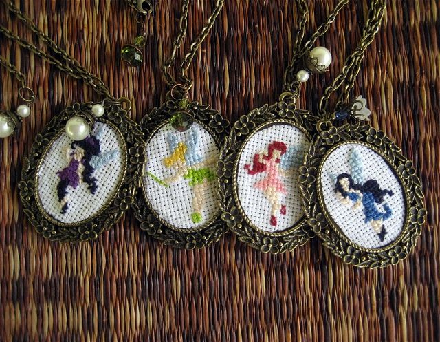 three necklaces with cross stitch designs on them sitting on a woven tablecloth covered surface