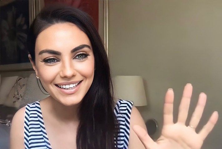 a woman with long black hair is smiling and waving her hand in front of the camera