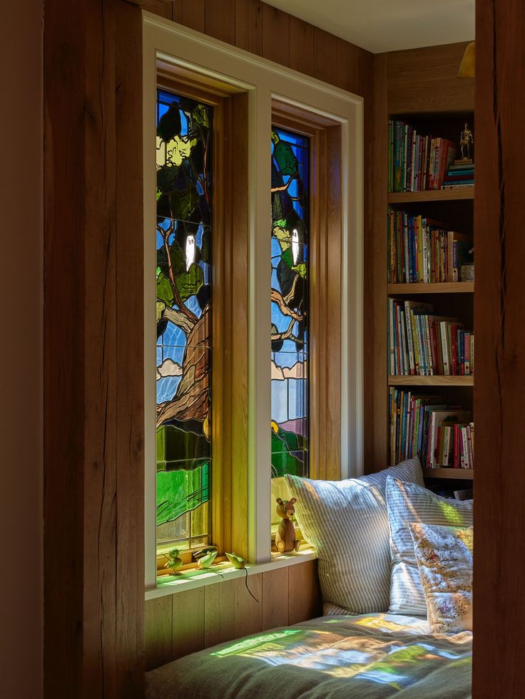 a bed sitting under two stained glass windows next to a book shelf filled with books