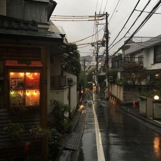 an empty street in the rain with power lines above it and buildings on both sides