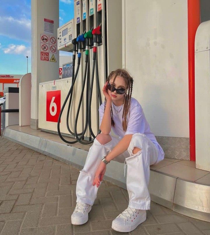 a woman sitting on the curb next to a gas station with her hand under her face