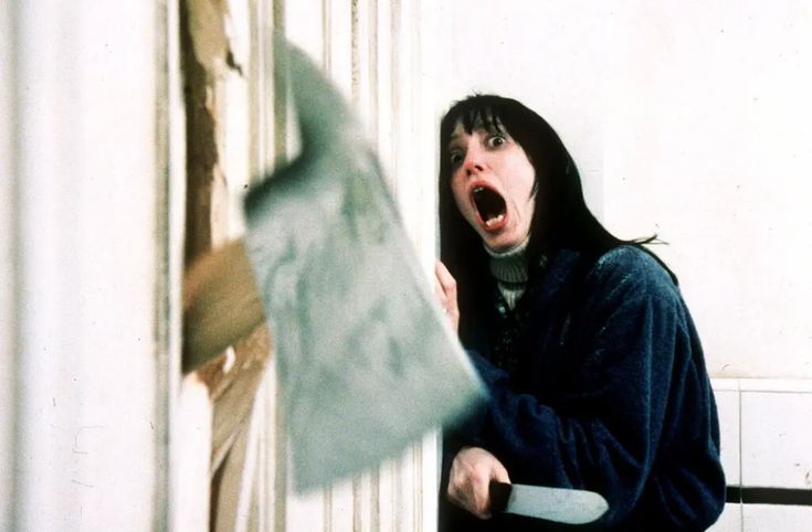 a woman holding an ax in front of a door with her mouth wide open and tongue out