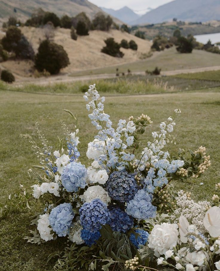 a vase filled with blue and white flowers sitting on top of a grass covered field