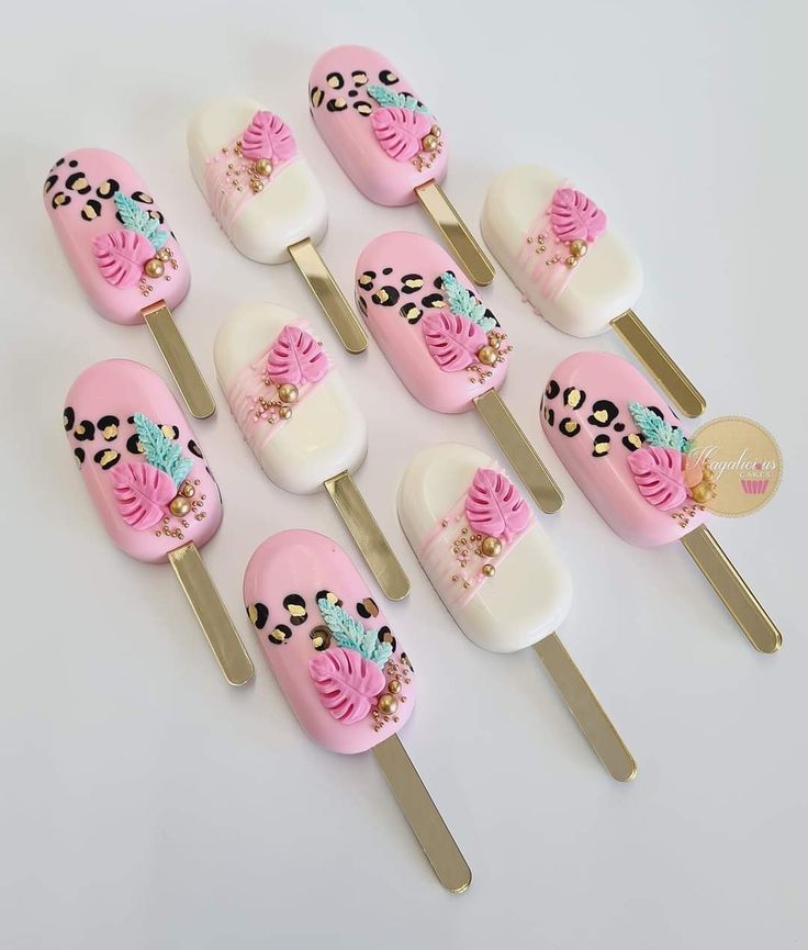 there are many pink and white cake pops with designs on them, along with gold forks