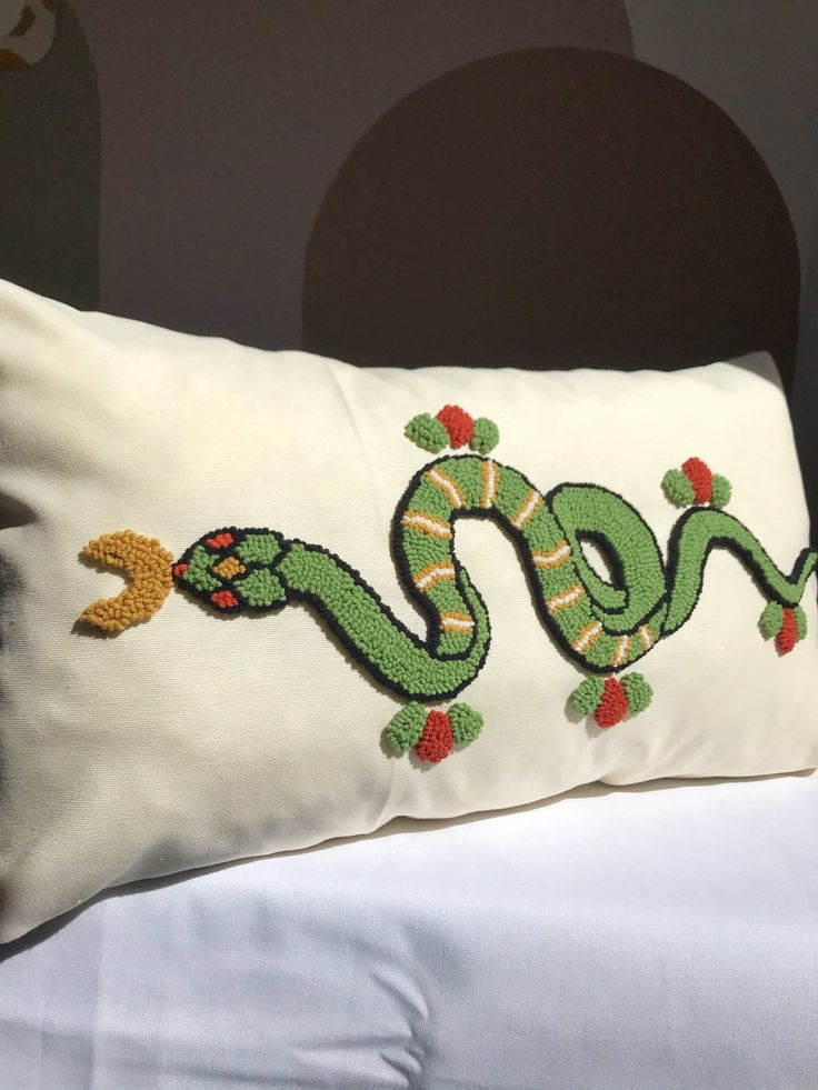 a white pillow with a green snake embroidered on the front and side, sitting on a bed