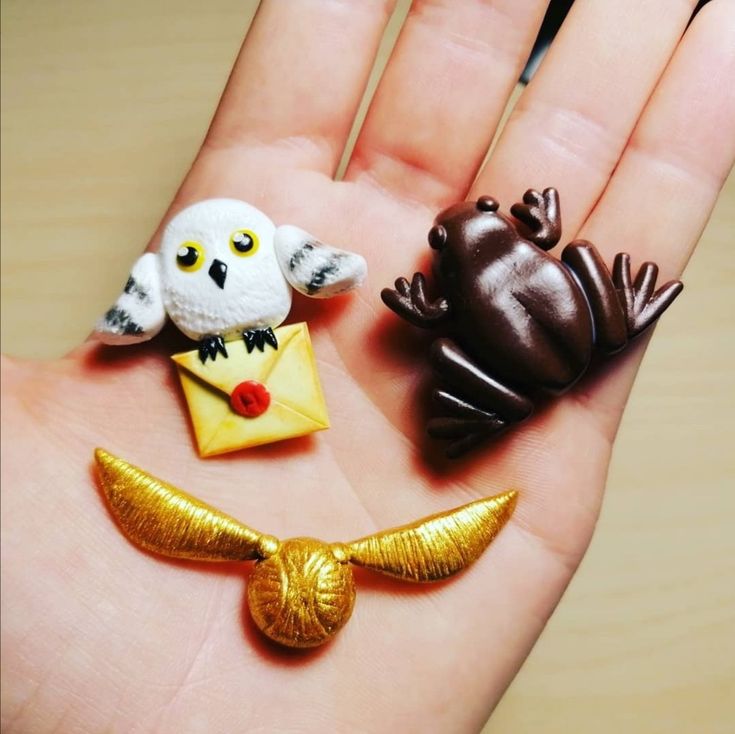 three small figurines in the palm of someone's hand, including an owl, frog and bird