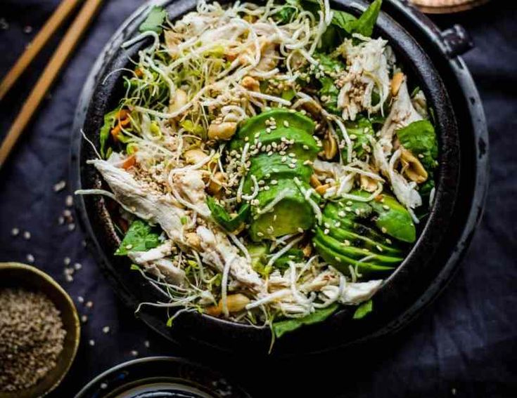 a bowl filled with salad next to chopsticks and other food on a table