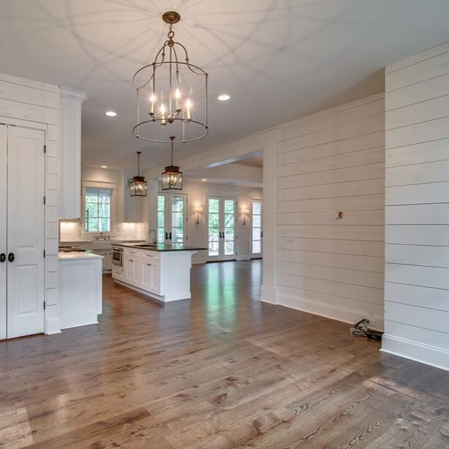 an empty kitchen and living room in a house with white walls, wood flooring and chandelier hanging from the ceiling