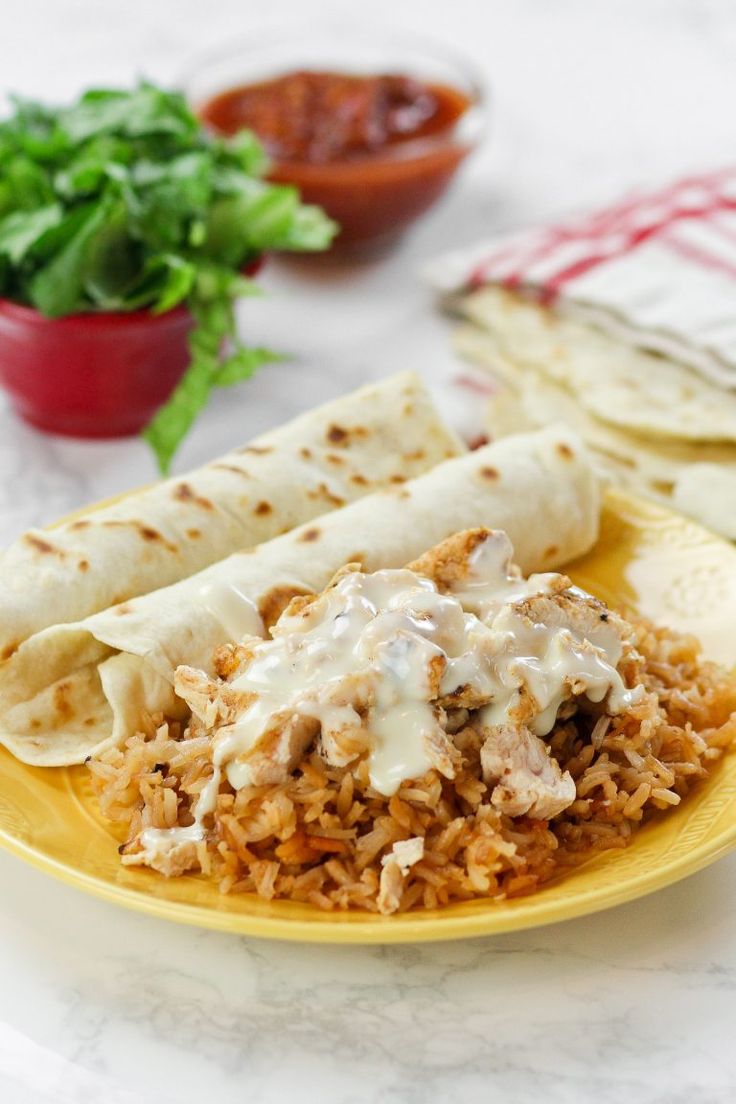 a yellow plate topped with burritos and rice covered in sauce next to lettuce