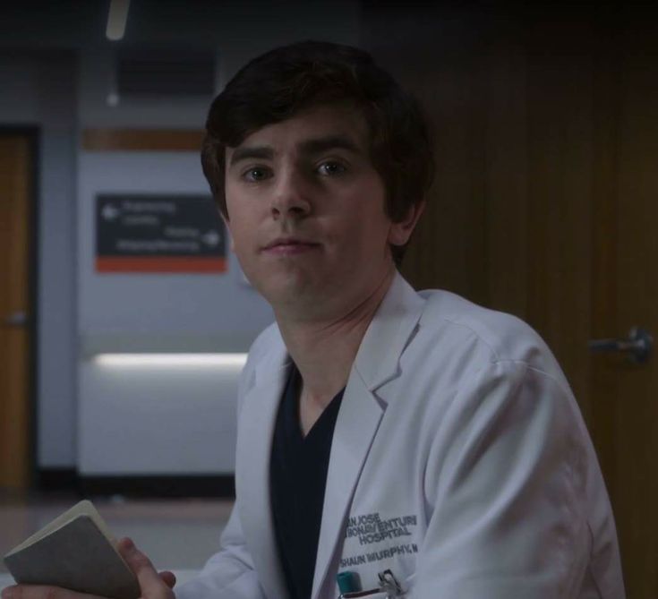 a male doctor in a white coat is holding a book and looking at the camera