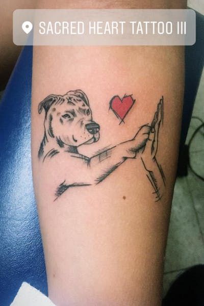 a tattoo on the arm of a woman with a dog holding a heart in her hand