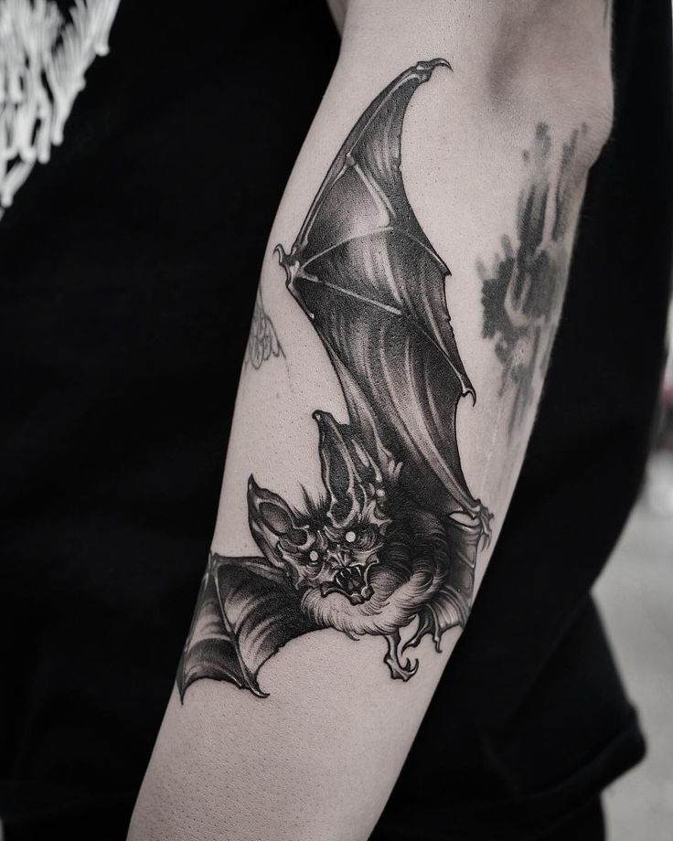 a black and white photo of a bat tattoo on the left upper half of the arm