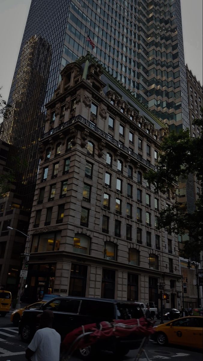 a tall building with lots of windows in the middle of a busy city street at dusk