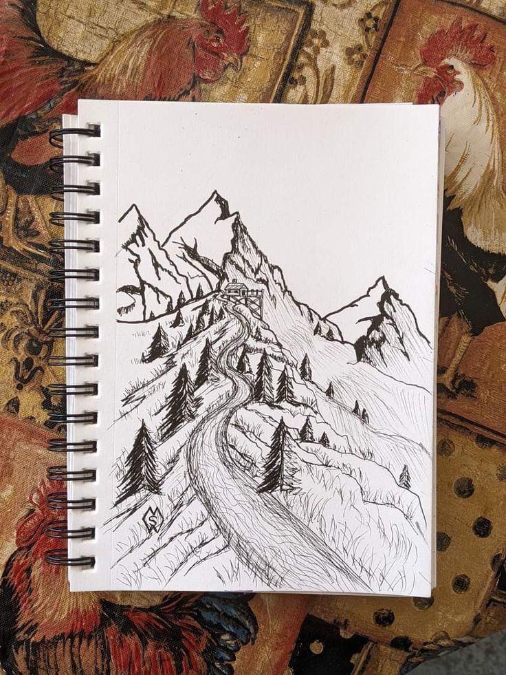 a notebook with a drawing of mountains and trees on the cover is sitting on a bed