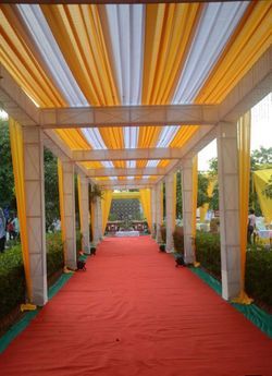 an orange and white wedding aisle with yellow draping on the sides, along with red carpet