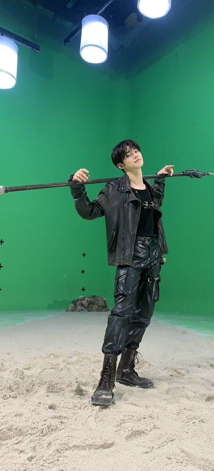 a man in black leather clothes is holding a large metal pole over his head while standing in front of a green screen