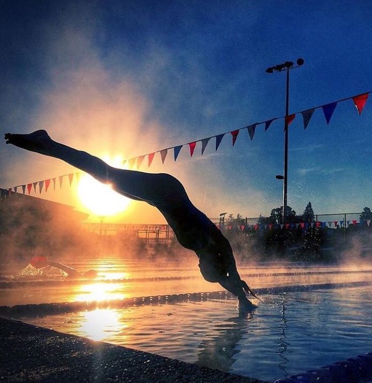 a person diving into a body of water with the sun setting in the back ground