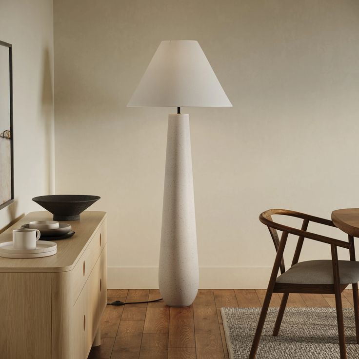 a tall white vase sitting on top of a wooden floor next to a table and chair