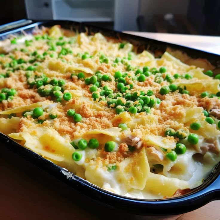 a casserole dish with peas and meat in it sitting on a wooden table