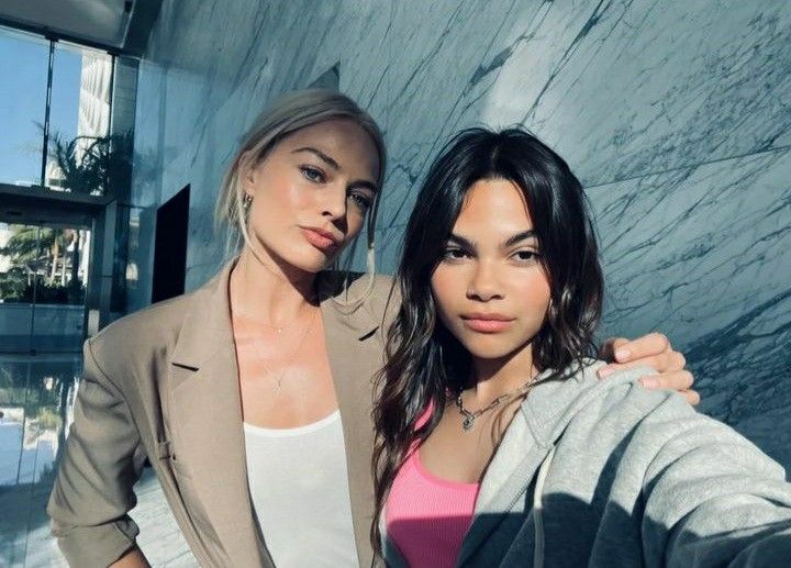 two beautiful women standing next to each other in front of a marble wall and building