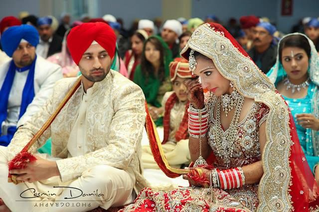 the bride and groom are sitting together in front of other people wearing red turbans