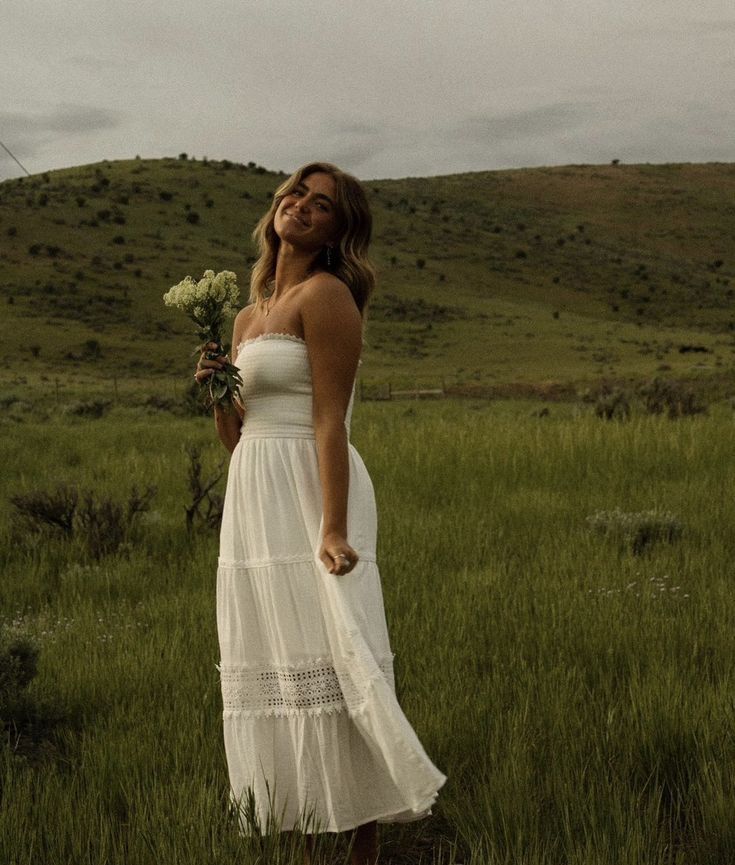 a woman in a white dress is standing in the grass with her eyes closed and flowers in her hand