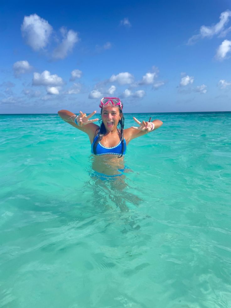 a woman standing in the ocean with her arms out and two fingers raised above her head