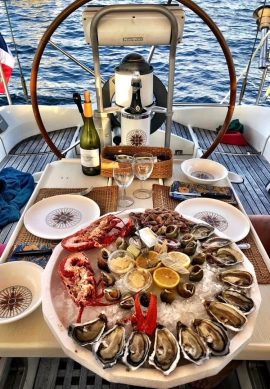 a large platter of oysters and wine on a sailboat in the ocean