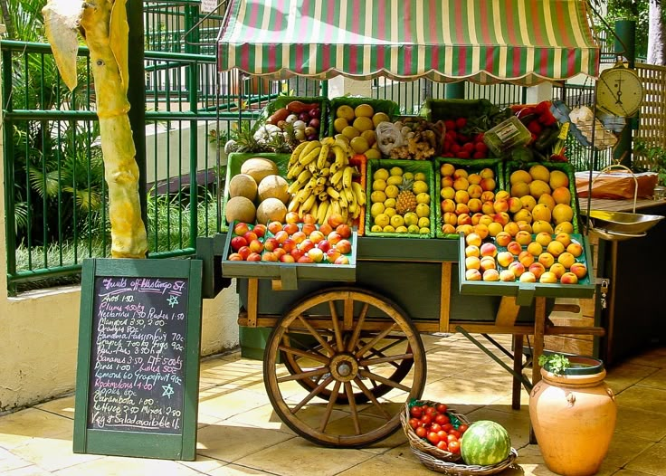 an outdoor fruit stand with various fruits and vegetables on it's display cart,