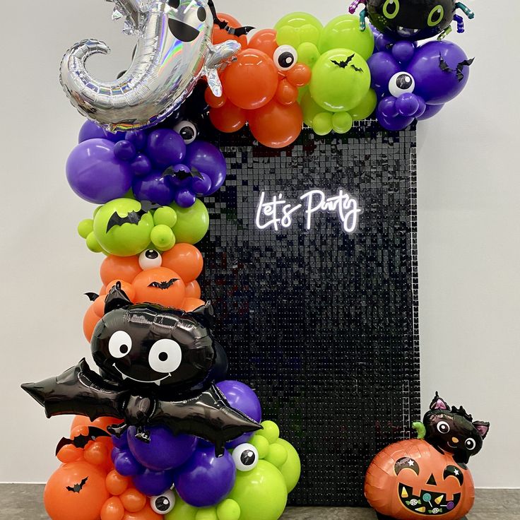 an assortment of halloween balloons and decorations in front of a blackboard with the words let's party written on it