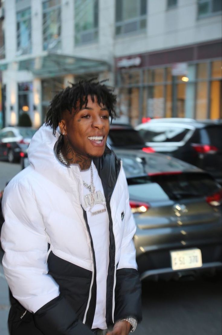 a man with dreadlocks is walking down the street in front of parked cars