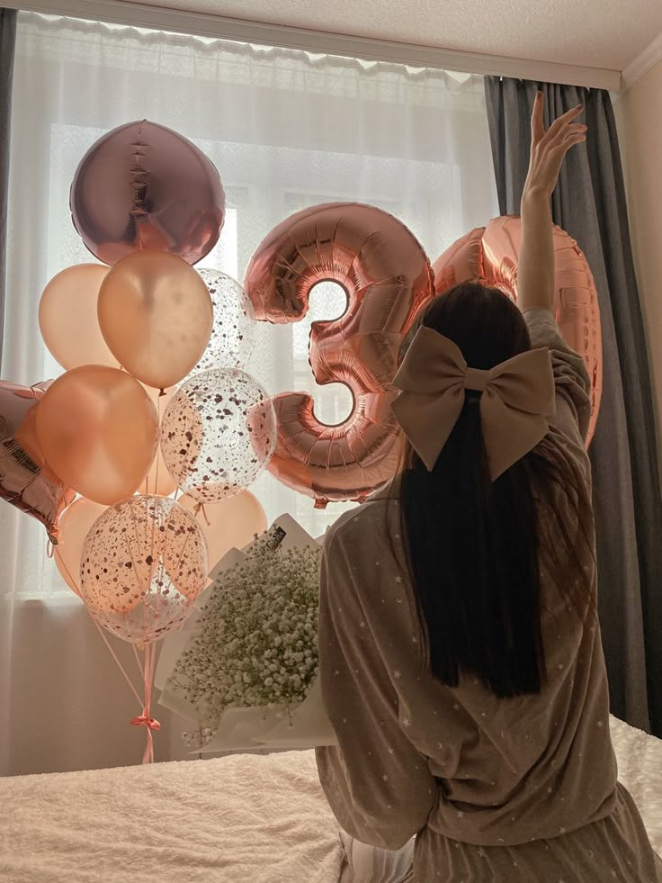 a woman sitting on top of a bed with balloons in the air above her head