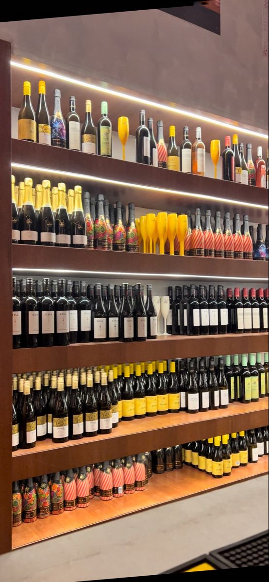 bottles of wine are lined up on shelves in a liquor store, with lights above them