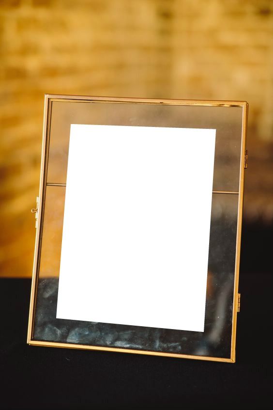 an empty photo frame sitting on top of a black cloth covered table with a brick wall in the background