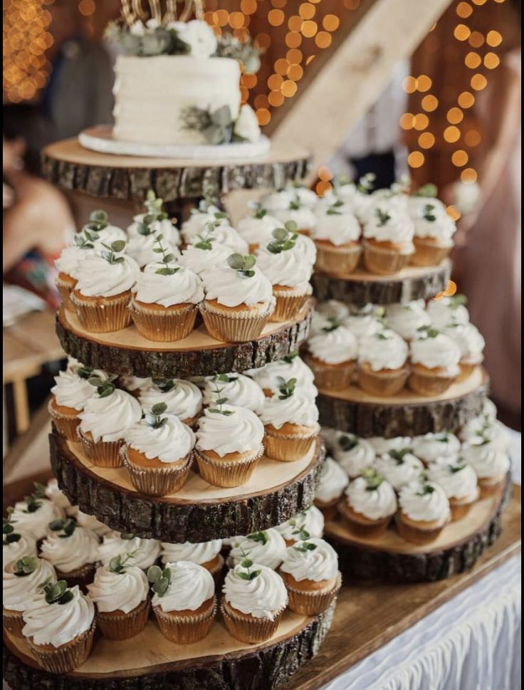 there are many cupcakes stacked up on the wooden table with lights in the background