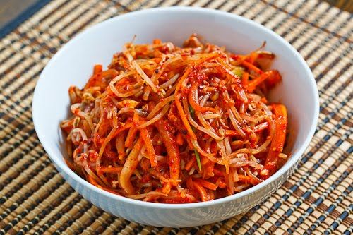 a white bowl filled with shredded carrots on top of a woven place mat next to a wooden table