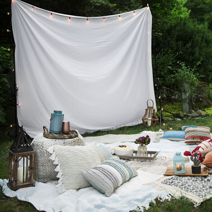 an outdoor area with pillows, blankets and lights on the grass in front of a white tarp