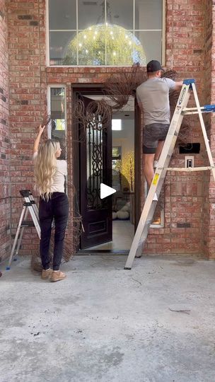 two people standing on ladders in front of a brick building while another person is painting the door