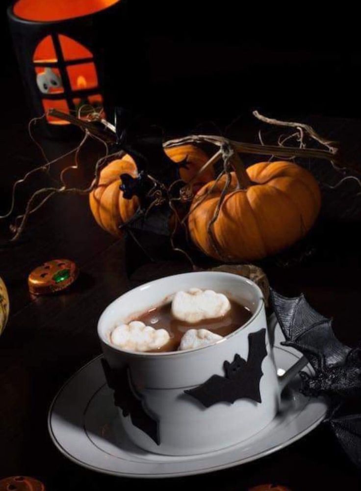 a white cup filled with hot chocolate on top of a table next to halloween decorations