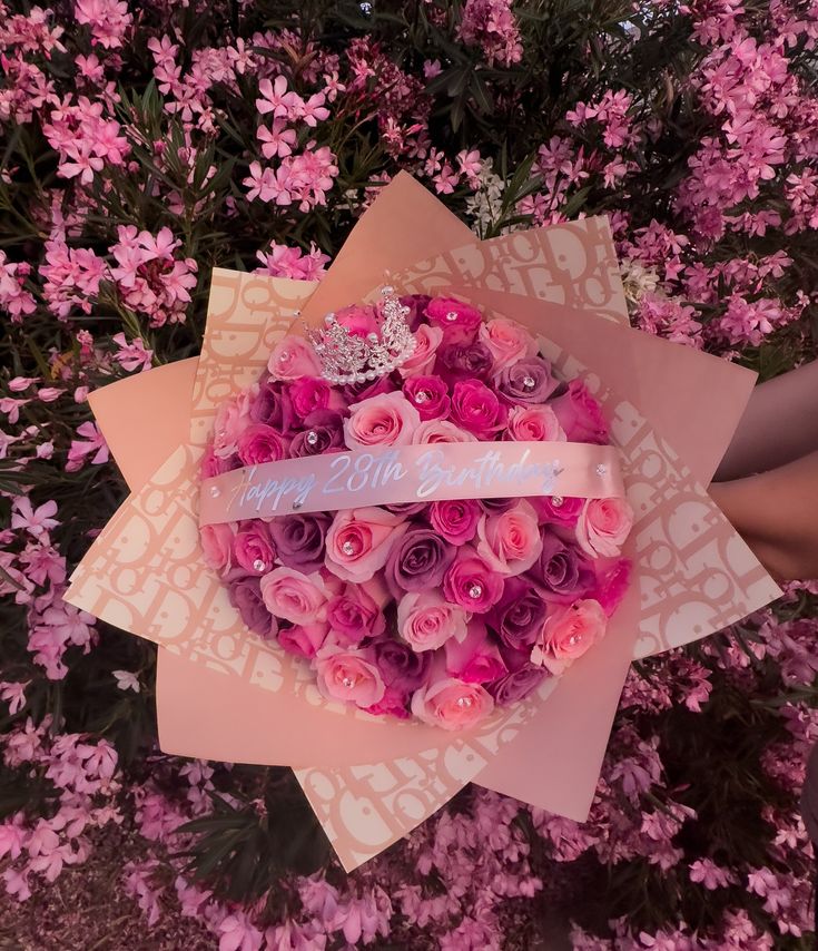 someone holding a bouquet of pink roses in front of purple flowers with a ribbon that says happy mother