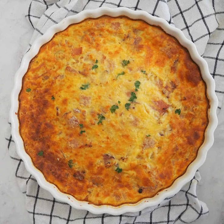 a cheesy casserole with meat and cheese in a white dish on a black and white checkered cloth