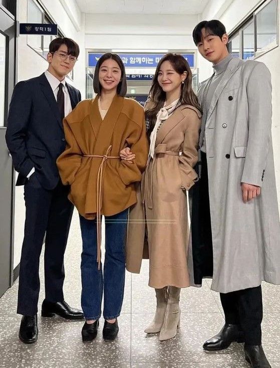 four people standing in an office hallway posing for a photo with one person wearing a trench coat