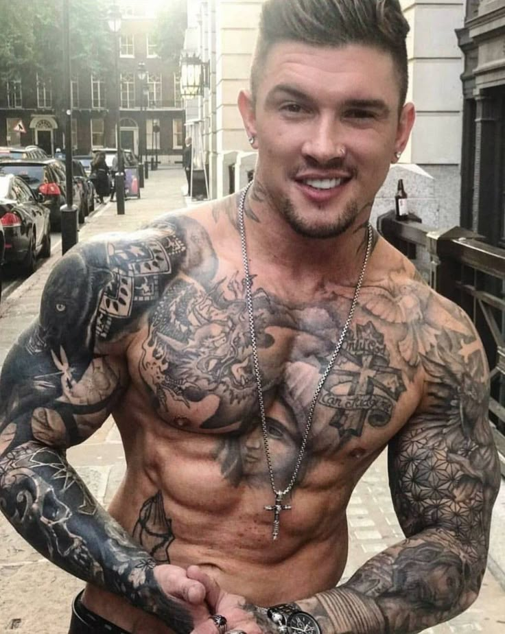 a shirtless man with tattoos on his chest and arm standing in front of a building