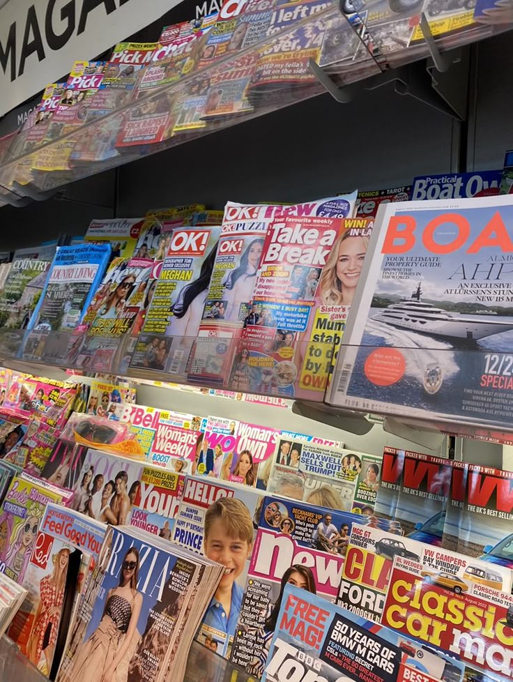 many magazines are stacked up on the shelves in a store, and one is being read